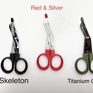 May include: Three medical shears in different colors: black with a skeleton design, red, and titanium green. The text "Red & Silver", "Skeleton", and "Titanium Green" are displayed.