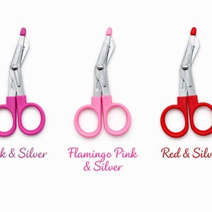 May include: Three medical shears with silver blades and colored handles. The handles are pink, light pink, and red. Text below reads "Pink & Silver", "Flamingo Pink & Silver", and "Red & Silver".