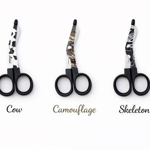 May include: Three pairs of black-handled scissors with decorative blades. Designs include a cow print, camouflage pattern, and a skeleton motif. The word "Cow", "Camouflage", and "Skeleton" are written below each pair of scissors.