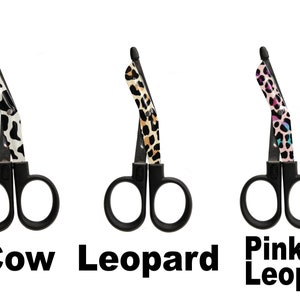 May include: Three pairs of black medical shears with patterned handles. The patterns include cow print, leopard print, and pink leopard print. The text "Cow", "Leopard", and "Pink Leopard" are below each pair of shears.