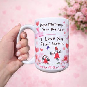 May include: White ceramic mug with a handle, decorated with pink hearts and floral designs. The mug features handwritten text that reads "Dear Mommy, Your the Best, I Love You From: Serena, Happy Mother's Day!" and children's drawings.