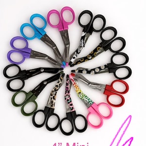 May include: A collection of 4-inch mini shears arranged in a circle. The scissors have black handles and blades, with colorful finger holes in various colors, including blue, pink, purple, and green. Some handles have decorative patterns.