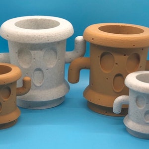 May include: Four different sized cactus-shaped planters, two are white and two are brown. The planters have a face with two eyes and a mouth.