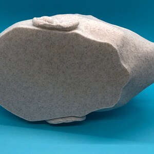 May include: A white ceramic sculpture of a head, viewed from the bottom. The sculpture has a textured surface and is shaped like a human head.