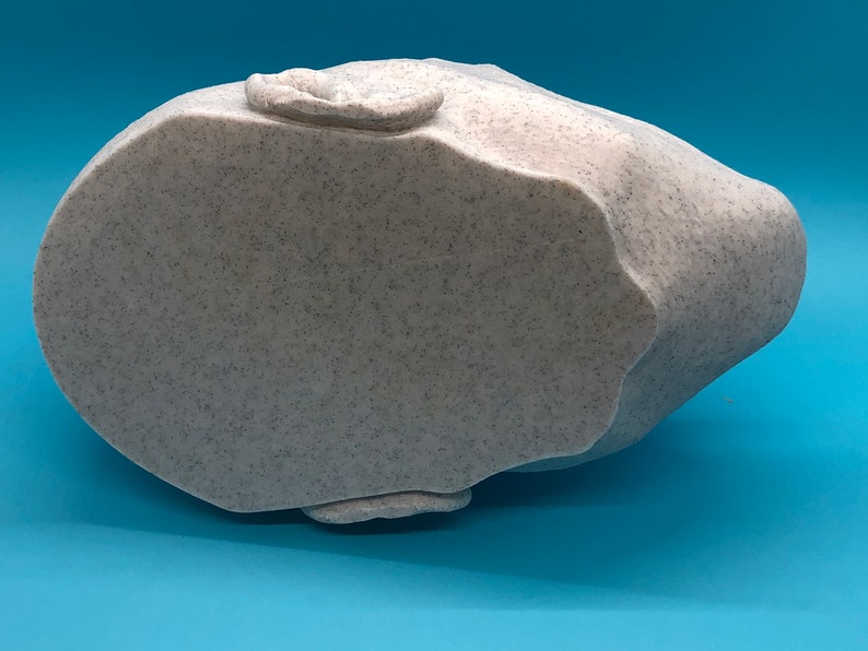 May include: A white ceramic sculpture of a head, viewed from the bottom. The sculpture has a textured surface and is shaped like a human head.