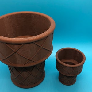 K&ouml;nnte beinhalten: Zwei braune, 3D-gedruckte Pflanzgef&auml;&szlig;e, eines gro&szlig; und eines klein, stehen auf einer blauen Oberfl&auml;che. Die Pflanzgef&auml;&szlig;e haben ein strukturiertes, gewebtes Korbmuster. Das gr&ouml;&szlig;ere Pflanzgef&auml;&szlig; ist etwa 18 cm hoch, das kleinere etwa 8 cm.