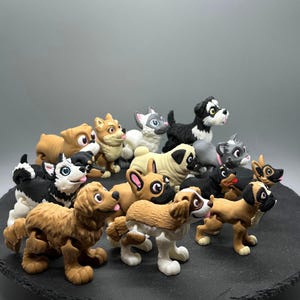 May include: A collection of 13 small, hand-painted figurines of dogs in various breeds and poses. The figurines are made of a light brown, gray, and black material and have realistic details.