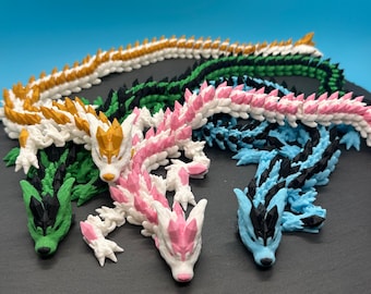 Könnte beinhalten: Vier farbenfrohe 3D-gedruckte Drachenfiguren mit stacheligen Rücken. Die Drachen sind in Gold-, Grün-, Rosa- und Blautönen gehalten.