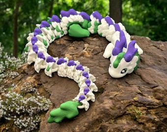 May include: A white and purple segmented dragon figurine with green accents. The dragon is curled up on a brown rock.
