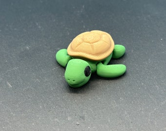 Könnte beinhalten: Eine kleine grüne und braune Schildkrötenfigur mit schwarzen Augen. Die Schildkröte ist aus Kunststoff und hat einen strukturierten Panzer.