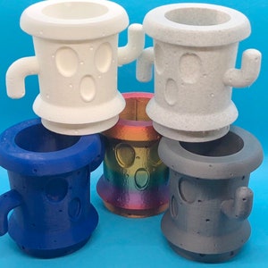 May include: Four 3D printed planters in different colors. Two are white with a textured surface and two are solid colors, one blue and one gray. Each planter has a unique design with two small holes and a handle on the side.