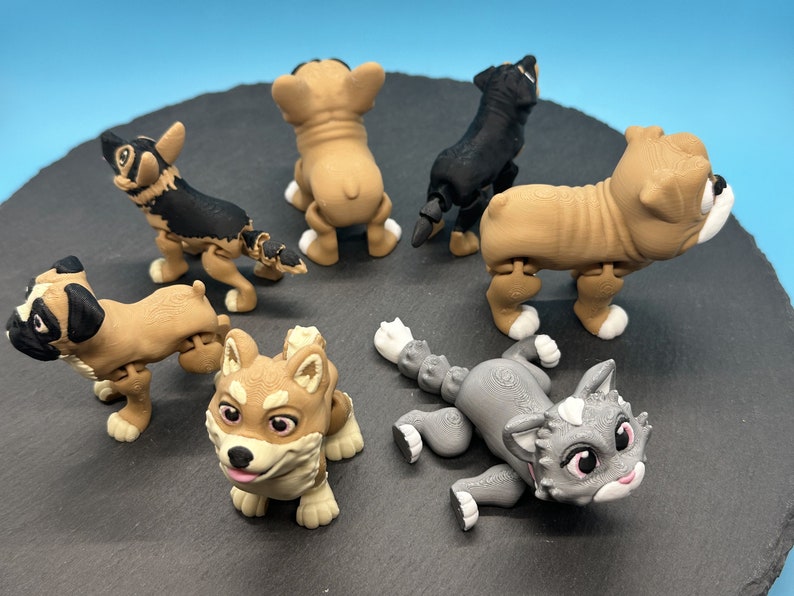 May include: A collection of six articulated animal figurines, including a bulldog, a pug, a husky, a french bulldog, a german shepherd, and a cat. The figurines are made of a brown, black, and gray plastic.
