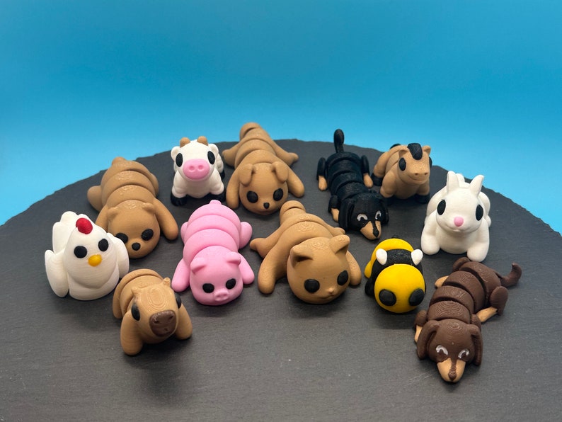 K&ouml;nnte beinhalten: Ein Set aus zehn Fondant-Tierfiguren, darunter eine Kuh, ein Schwein, eine Biene, ein Huhn, eine Katze, ein Hund und ein Kaninchen. Die Figuren sind alle in einer zusammengerollten Position und sollen schlafend aussehen. Die Figuren befinden sich auf einer schwarzen Oberfl&auml;che.