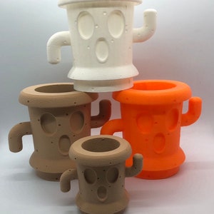 May include: Four cactus-shaped planters in different sizes. The largest planter is white, the next largest is brown, the next is orange, and the smallest is brown. All planters have a face with two eyes and a mouth.