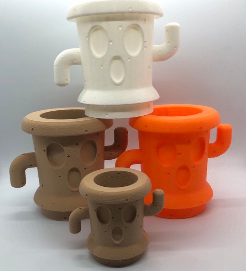 May include: Four cactus-shaped planters in different sizes. The largest planter is white, the next largest is brown, the next is orange, and the smallest is brown. All planters have a face with two eyes and a mouth.