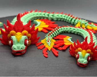 May include: Two green and red dragon figurines with intricate details. The dragons have a segmented body and a large head with a red and yellow crown.