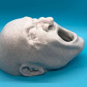May include: A white, 3D printed sculpture of a face with an open mouth, as if screaming. The sculpture is textured and has a rough surface.