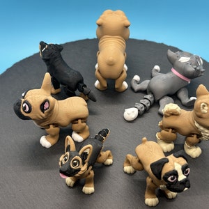 May include: Six small, articulated, plastic dog figurines. The dogs are in various poses and are made of brown, black, and gray plastic. The figurines are on a black surface.