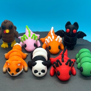 K&ouml;nnte beinhalten: Eine Sammlung von acht kleinen, bunten, 3D-gedruckten Tierfiguren. Die Figuren umfassen einen Truthahn, einen Fuchs, einen Panda, eine Raupe, einen roten Drachen, einen orangefarbenen Drachen, einen rosa Drachen und eine schwarze Fledermaus.