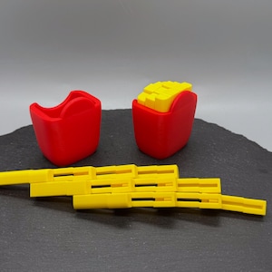 May include: A set of 3D-printed toys resembling fast food items. The set includes a red container, a container of fries, and a yellow, articulated toy. The fries are yellow and the containers are red.