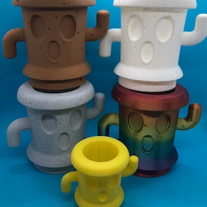 May include: Four different colored cactus-shaped planters with a cartoon face. The planters are made of a textured material and are in various colors, including brown, white, gray, and yellow.