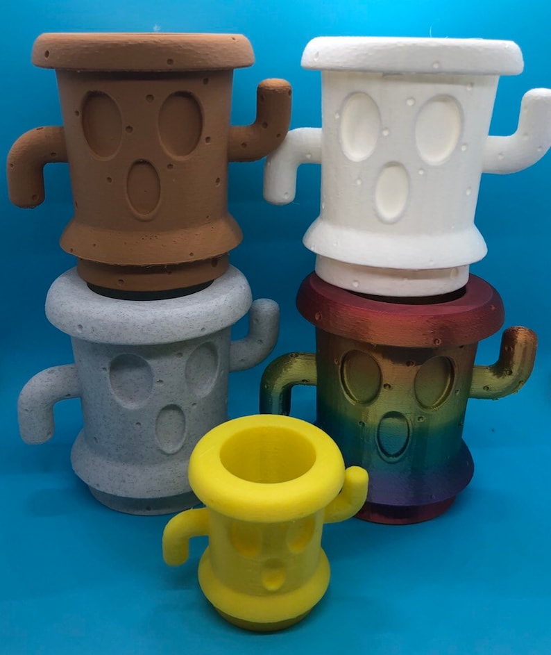 May include: Four different colored cactus-shaped planters with a cartoon face. The planters are made of a textured material and are in various colors, including brown, white, gray, and yellow.