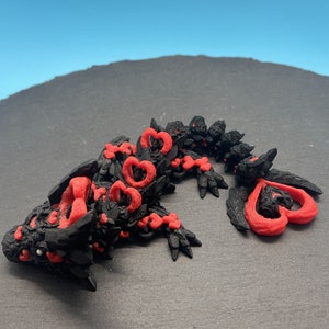 Op de afbeelding: Een zwart en rood 3D-geprint drakenbeeldje met hartvormige details. De draak ligt op zijn zij met zijn kop naar de zijkant gedraaid.