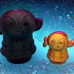 May include: Two stylized figurines with a tribal design. One is dark purple, the other is gold with purple accents. They have large ears and outstretched arms. The background is a blue gradient with sparkling details.