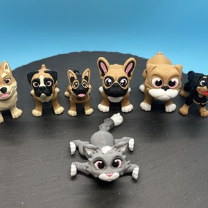 May include: A collection of seven small, hand-painted figurines of dogs and a cat. The figurines are all different breeds and have realistic features. They are all standing on a black surface.