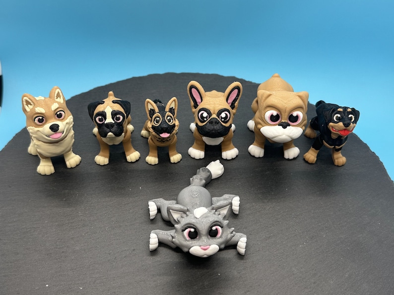 May include: A collection of seven small, hand-painted figurines of dogs and a cat. The figurines are all different breeds and have realistic features. They are all standing on a black surface.