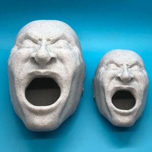 May include: Two white, textured, 3D printed sculptures of human faces with open mouths. The sculptures are facing the camera and are on a blue background.
