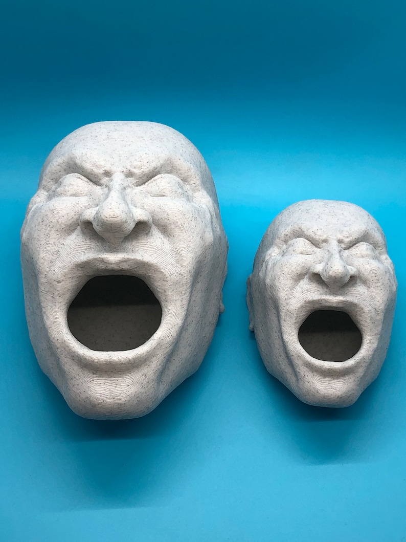May include: Two white, textured, 3D printed sculptures of human faces with open mouths. The sculptures are facing the camera and are on a blue background.