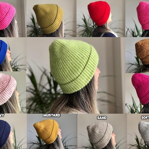 Pode incluir: Uma coleção de dez gorros de malha em várias cores, incluindo rosa, mostarda, areia, cinza suave, azul marinho e verde. Os gorros são todos feitos de um material macio e quente e têm uma textura canelada.