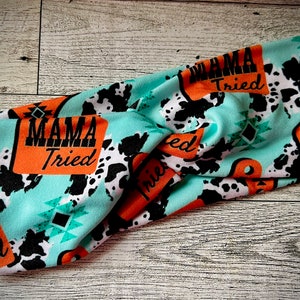May include: Turquoise blue headband with a cow print and orange signs that say "Mama Tried".