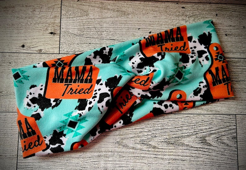 May include: Turquoise blue headband with a cow print and orange signs that say "Mama Tried".