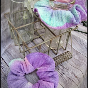 May include: Two glass jars with a pastel blue, pink, and purple scrunchie on top of them. The jars are in a metal wire rack. The scrunchie is made of a soft, stretchy fabric.