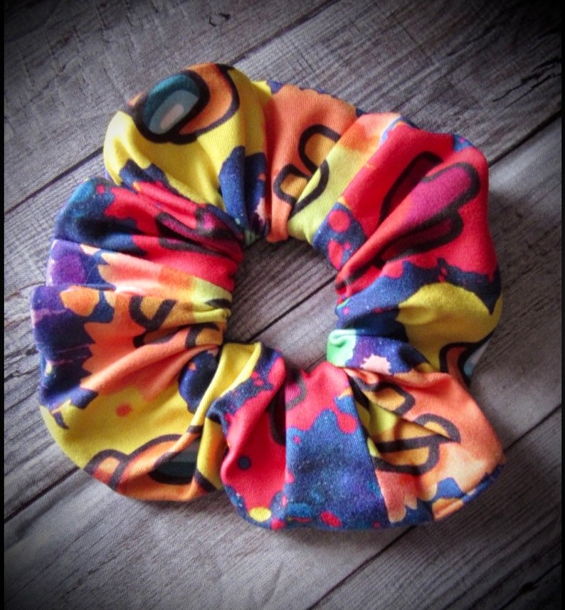 May include: A colorful scrunchie with a tie-dye pattern featuring yellow, red, blue, and black. The scrunchie has a repeating pattern of cartoon characters.