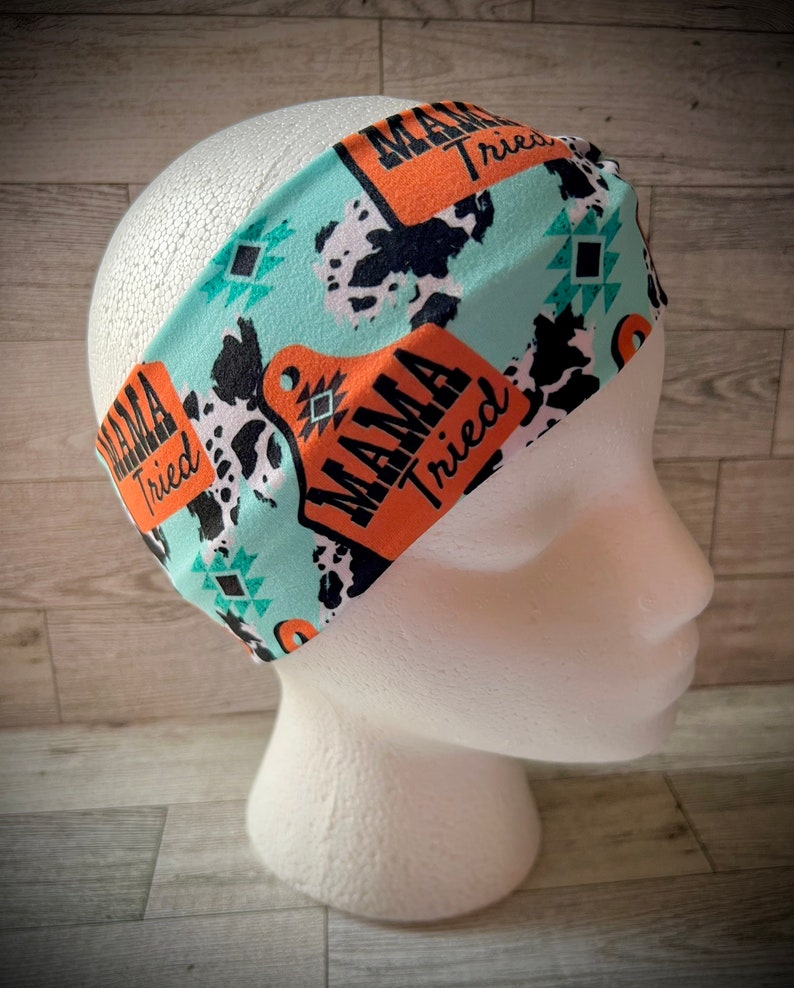 May include: Turquoise headband with a cow print and orange "Mama Tried" text.