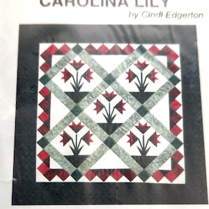 May include: A sewing pattern packet titled Little Bits Carolina Lily by Cindi Edgerton, featuring a graphic of a quilt with red flowers and green lattice on a black background. The text states it includes tissue paper foundations for making one 30 3/8" x 30 3/8" wall quilt.