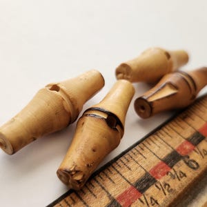 May include: Four small, light-colored wooden whistles with a ruler. The whistles have a cylindrical shape with a flared end. The ruler is made of wood and has black and red markings.
