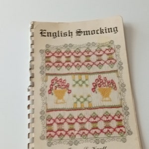 May include: A vintage book titled "English Smocking" by Grace L. Knott. The cover features a colorful embroidered design with floral motifs and geometric patterns.