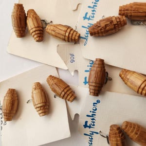 May include: A selection of vintage wooden barrel-shaped buttons, with metal shanks for sewing. The buttons are a warm brown hue and are attached to off-white paper cards. The cards feature the text "Lady Fashion".