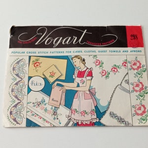 May include: A vintage cross stitch pattern booklet with a woman wearing a pink apron and holding a towel. The cover features the title "Vogart Transfer Pattern" and the number "298". The booklet includes patterns for cases, cloths, guest towels, and aprons.