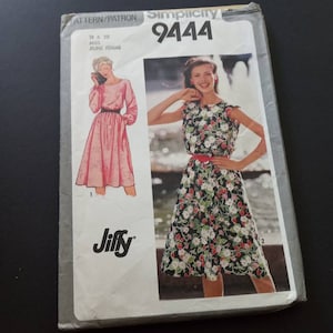 May include: Simplicity sewing pattern number 9444 for a dress. The pattern is for sizes 18 and 20, and is labeled as "Miss/Jeune Femme". The pattern shows two different styles of dresses, one with long sleeves and a solid pink color, and the other with short sleeves and a floral print.