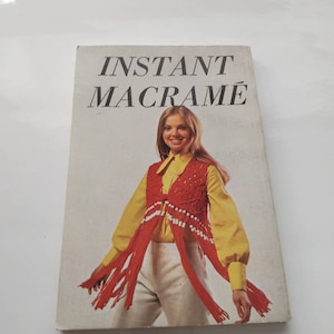 May include: A book titled "Instant Macrame" featuring a woman wearing a red macrame vest with white beads and a yellow shirt on the cover.