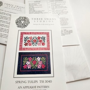 Puede incluir: Un folleto de instrucciones para el patrón de aplique Spring Tulips TSS 3040 de Three Swans Studios. La portada presenta dos diseños florales rectangulares con tulipanes rojos, rosas y verdes sobre fondos texturizados en rojo y azul oscuro.