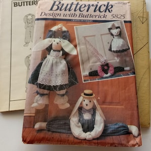 Könnte beinhalten: Ein Vintage-Butterick-Schnittmuster für Hasenpuppen, Design 5825. Das Cover zeigt Illustrationen der fertigen Puppen, darunter ein Hase mit Kleid und Schürze und ein weiterer in Latzhosen. Zusätzliche Schnittmusterbögen sind sichtbar.