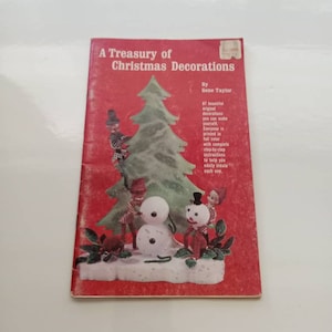 Puede incluir: Un libro vintage titulado "A Treasury of Christmas Decorations" de Gene Taylor. La portada presenta una ilustración colorida de un árbol de Navidad, muñecos de nieve y duendes.