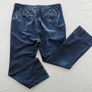 May include: Dark blue denim pants with a classic five-pocket design. The pants have a button and zipper closure, belt loops, and two back pockets. The legs are straight with a slight flare at the hem.