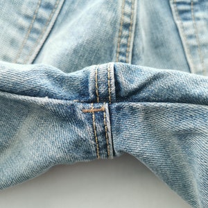 May include: Close-up of light blue denim jeans, showcasing the detailed stitching and fabric texture. The image highlights the seams and the worn appearance of the denim, emphasizing the garment's construction and style.